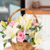 Cesta de mimbre con lirios blancos, rosas rosadas, hojas verdes y alstroemeria blanca